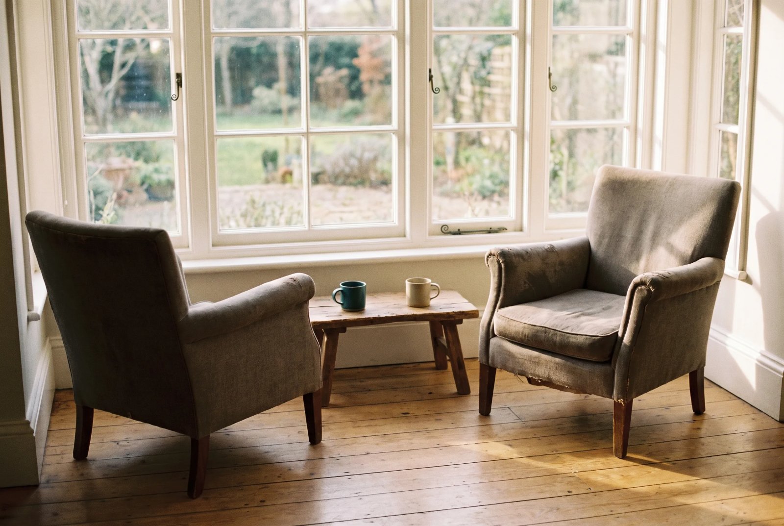 Two empty chairs turned toward each other beside a sunlit window
