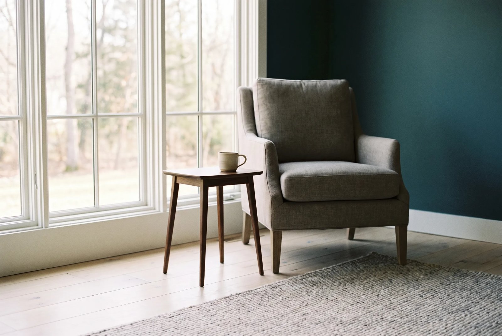 An empty linen armchair beside a sunlit window in a quiet room