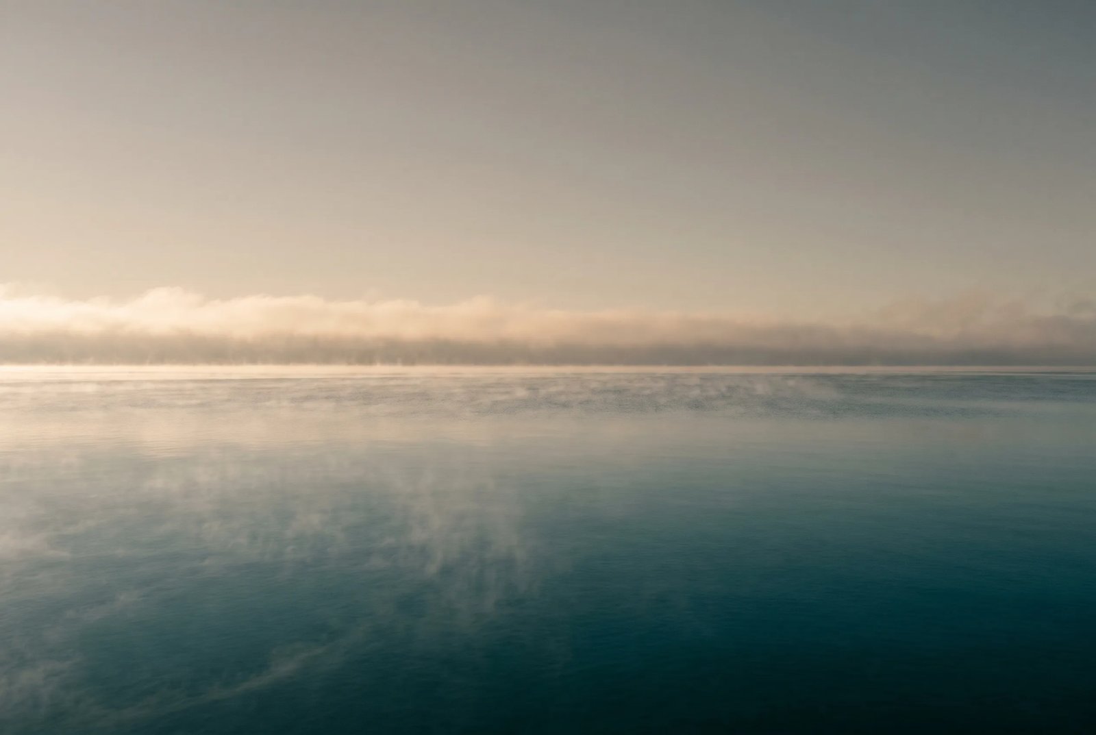 Still open water at first light with mist lifting from a calm horizon